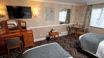 A hotel room with two beds, a TV, a dresser, a mirror, a small table, and a window with curtains.