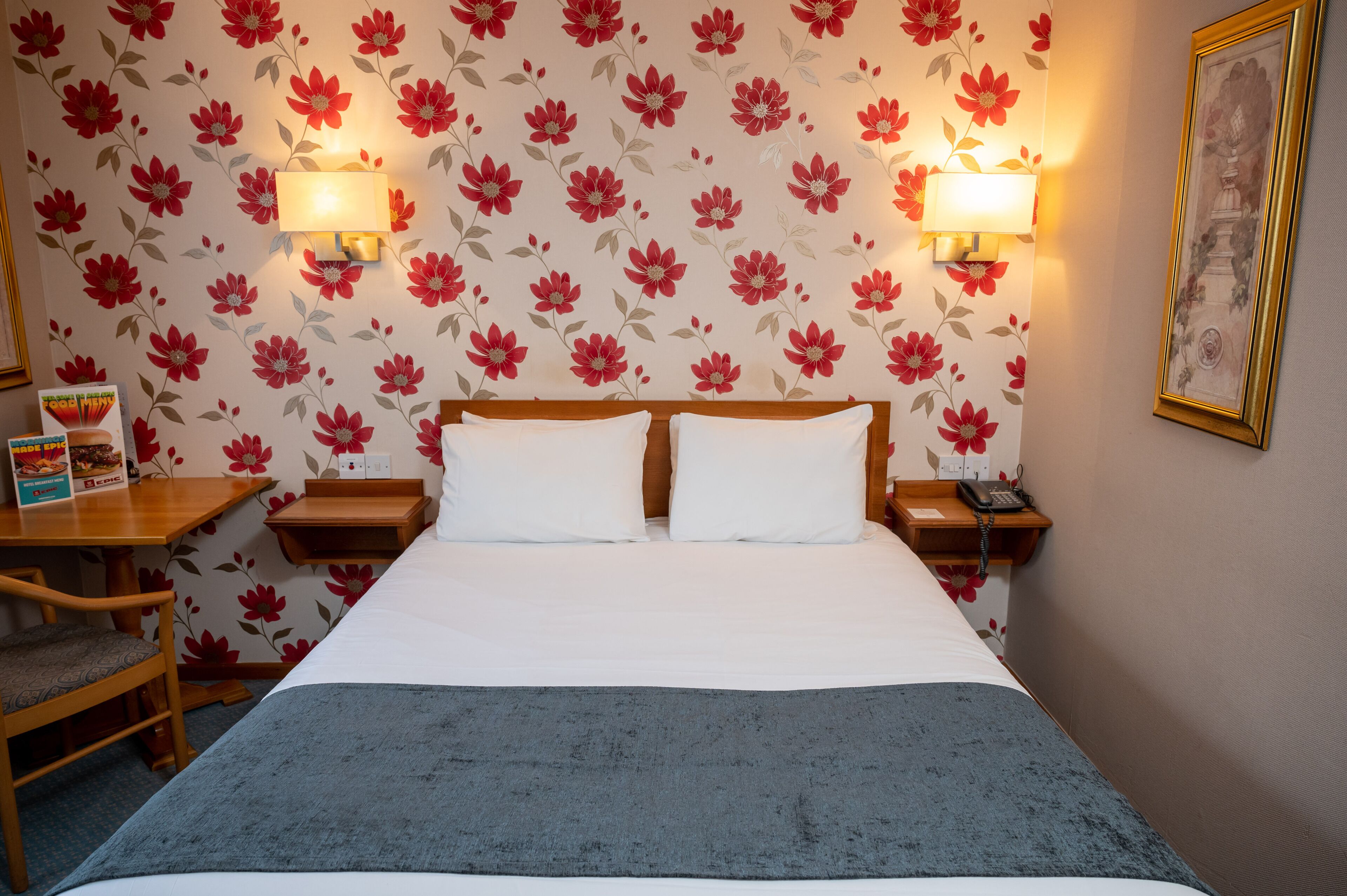 A hotel room with a bed, two bedside tables, a chair, a desk, and a lamp.