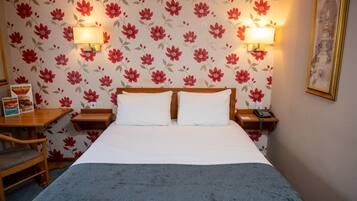 A hotel room with a bed, two bedside tables, a chair, a desk, and a lamp.