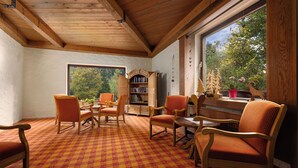 A cozy room with wooden furniture, a checkered carpet, and a large window offering a view of trees.