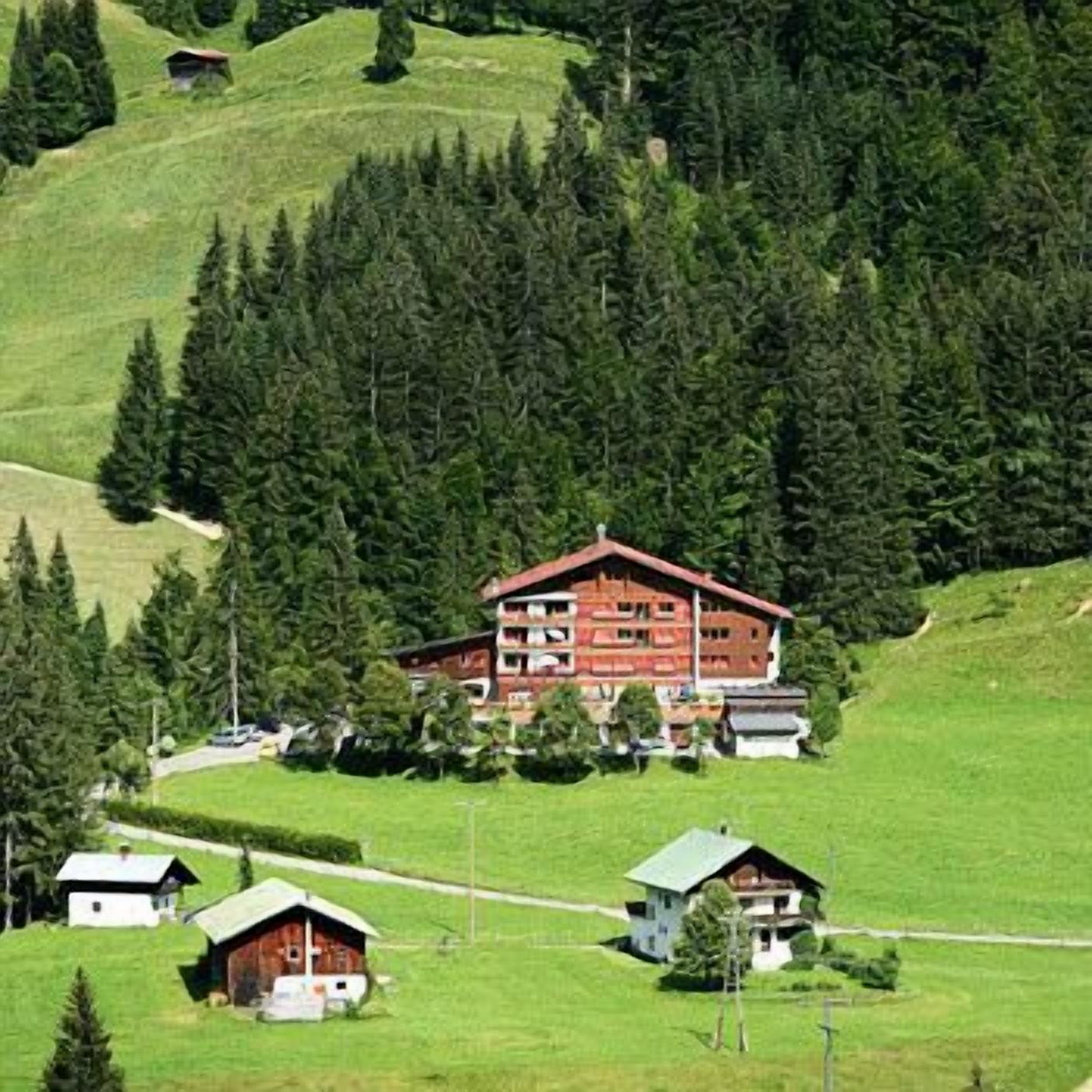 A large red building with multiple balconies, surrounded by green fields and trees.