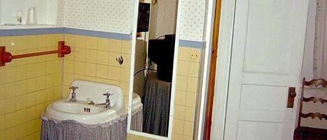 A small, compact room with a single bed, a bedside table, a mirror, and a bathroom with a sink and toilet.