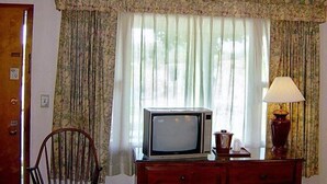 A room with a television on a wooden dresser, a chair, and a lamp. - West Road Motel (Bennington)