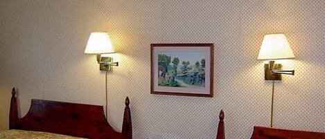 A hotel room with two beds, a nightstand with a lamp, a framed picture on the wall, and a telephone.