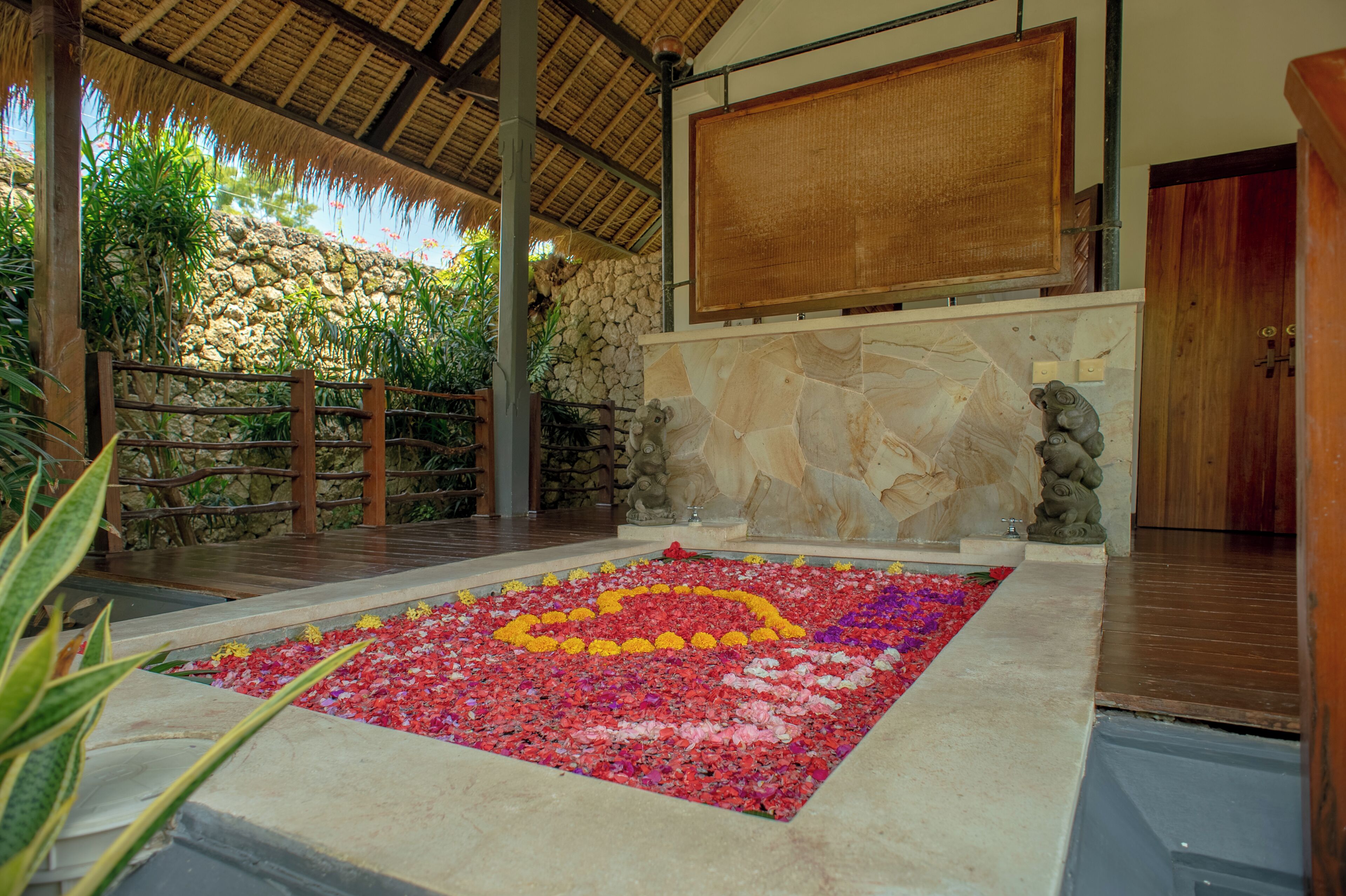 Una habitación con pared de piedra, un banco de madera y un arreglo floral decorativo.
