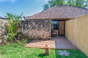 Un edificio de paredes de piedra con techo de tejas, un muelle de madera y un pequeño espacio al aire libre con mesas y sillas.