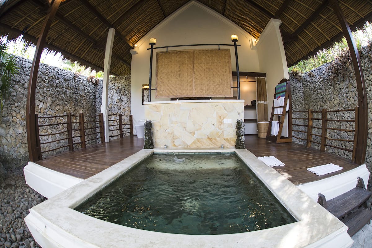 Un espacio de spa con pared de piedra, terraza de madera y una bañera de hidromasaje.