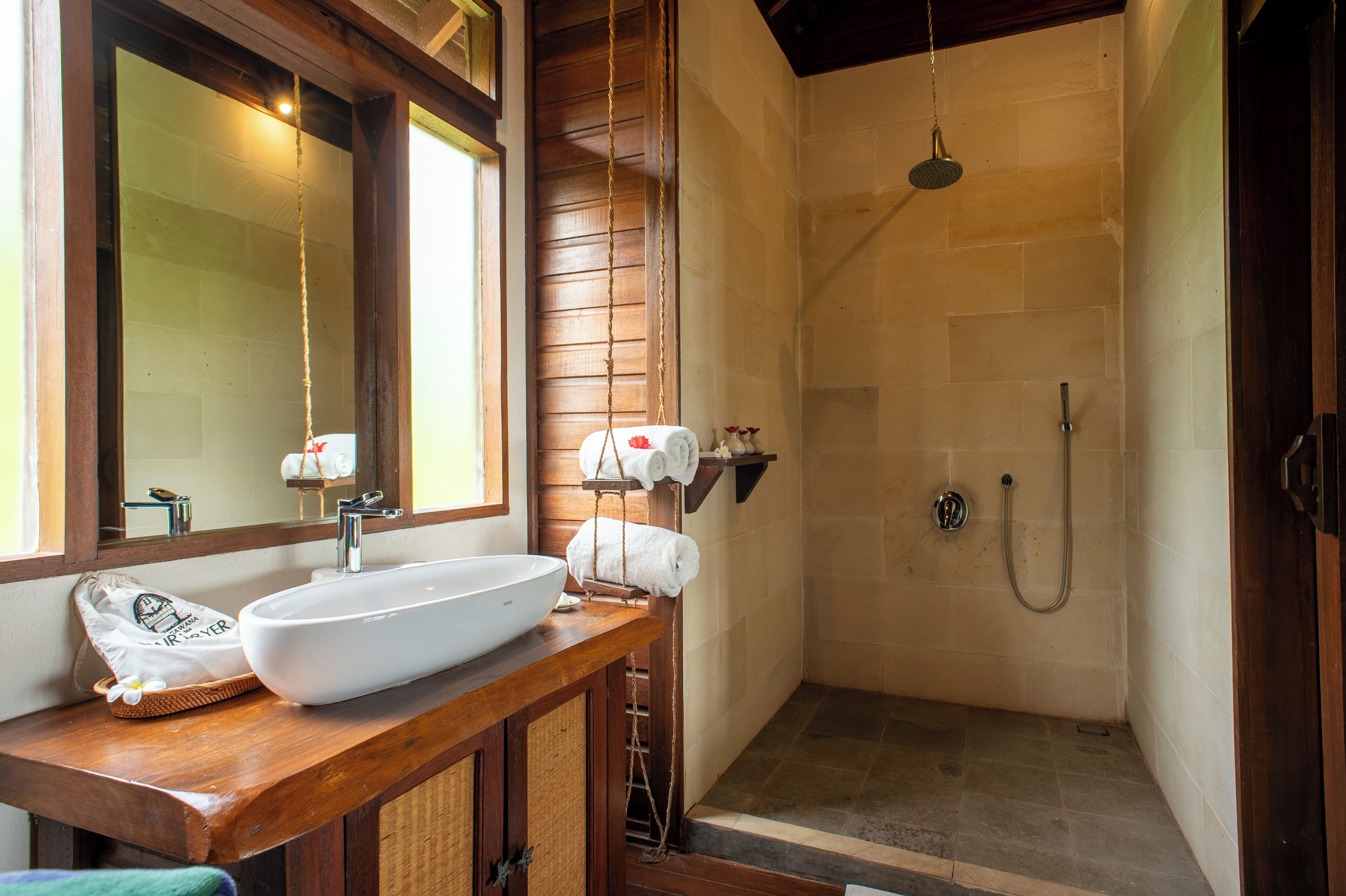 Een badkamer met een houten wastafel, een witte wasbak, een spiegel, een handdoekhouder en een douche.