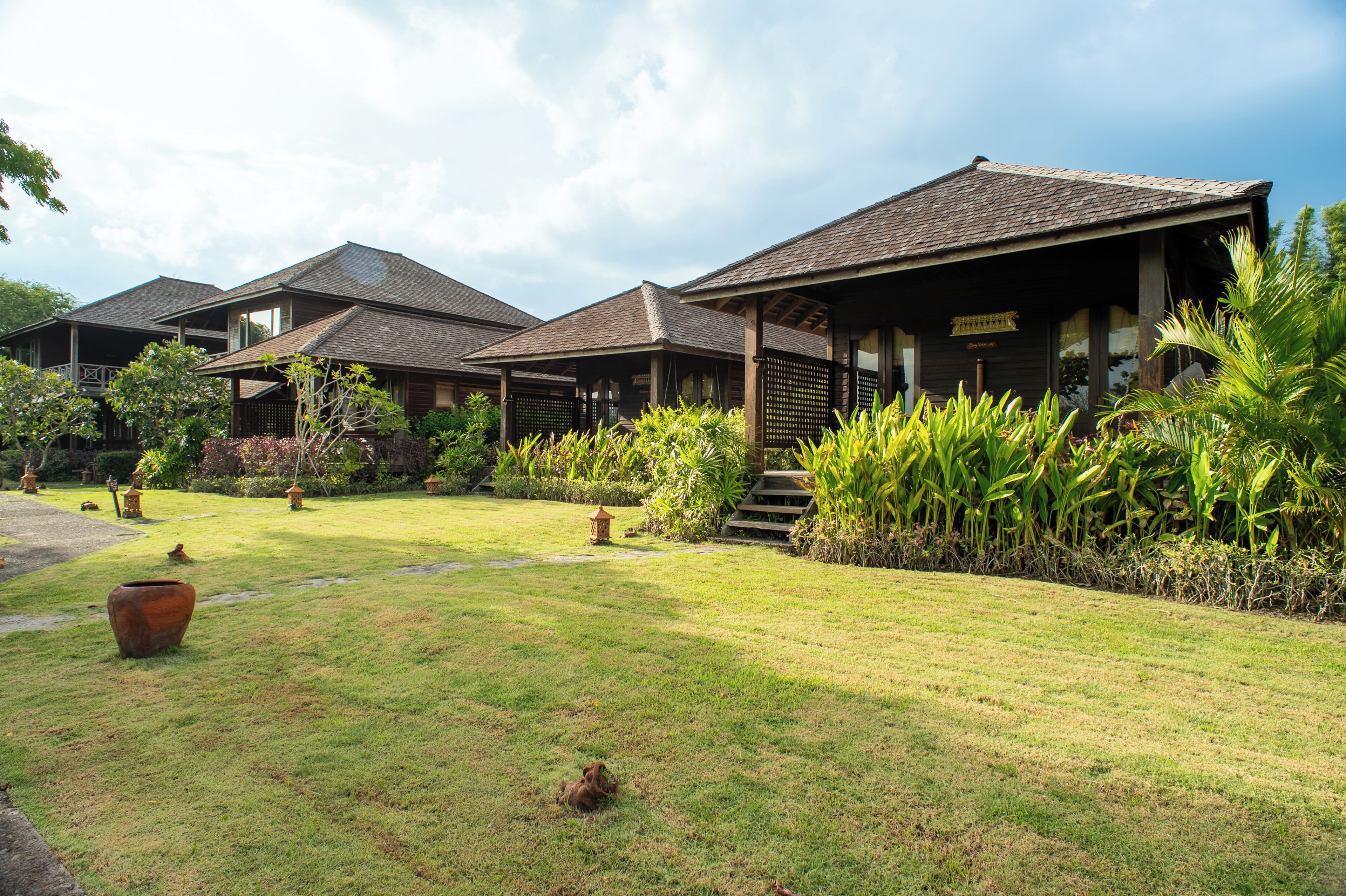Een traditioneel houten gebouw met een overdekte veranda, omringd door weelderige begroeiing en een verzorgd gazon.