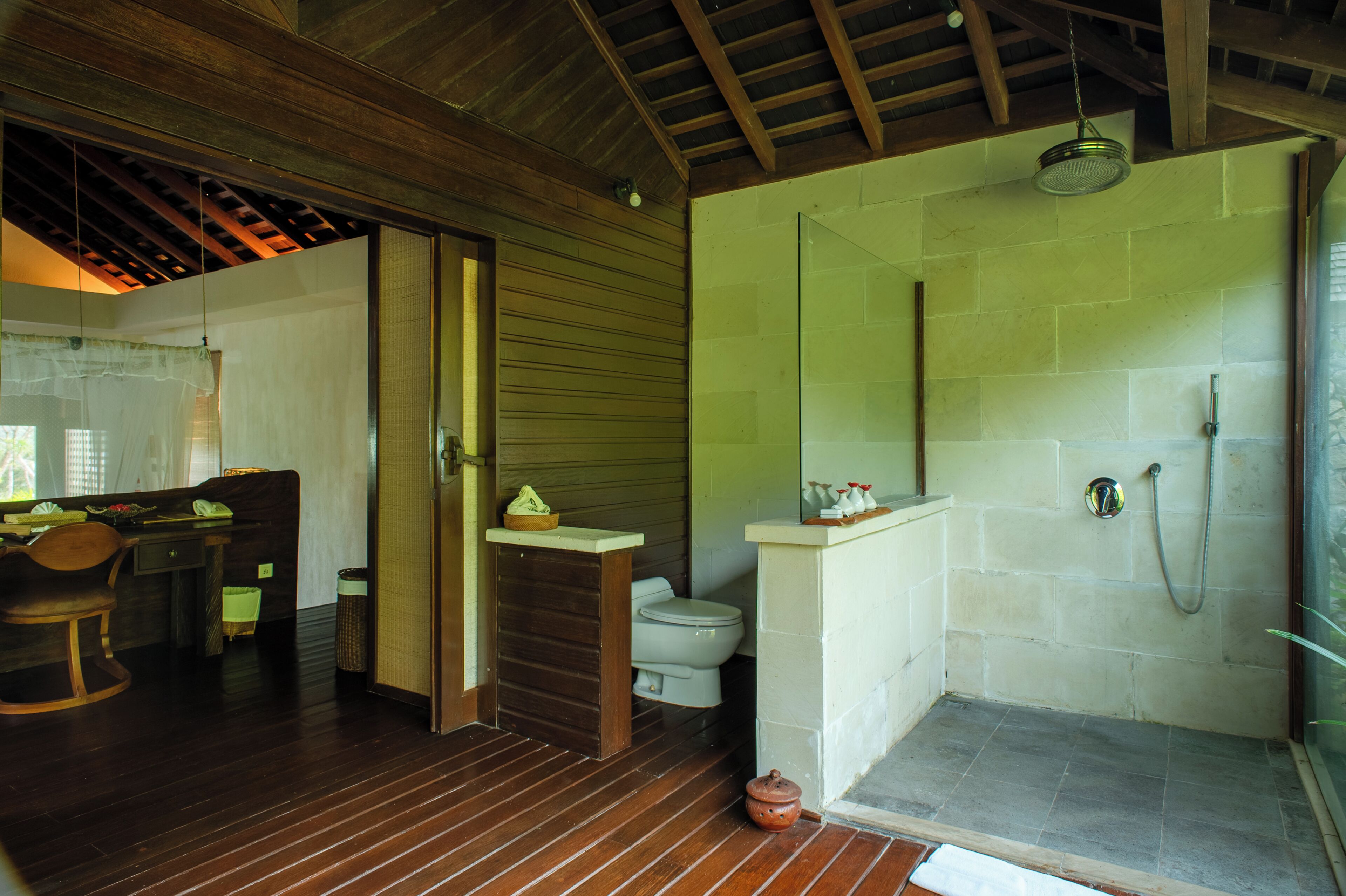 A bathroom with a shower, toilet, and wooden flooring.