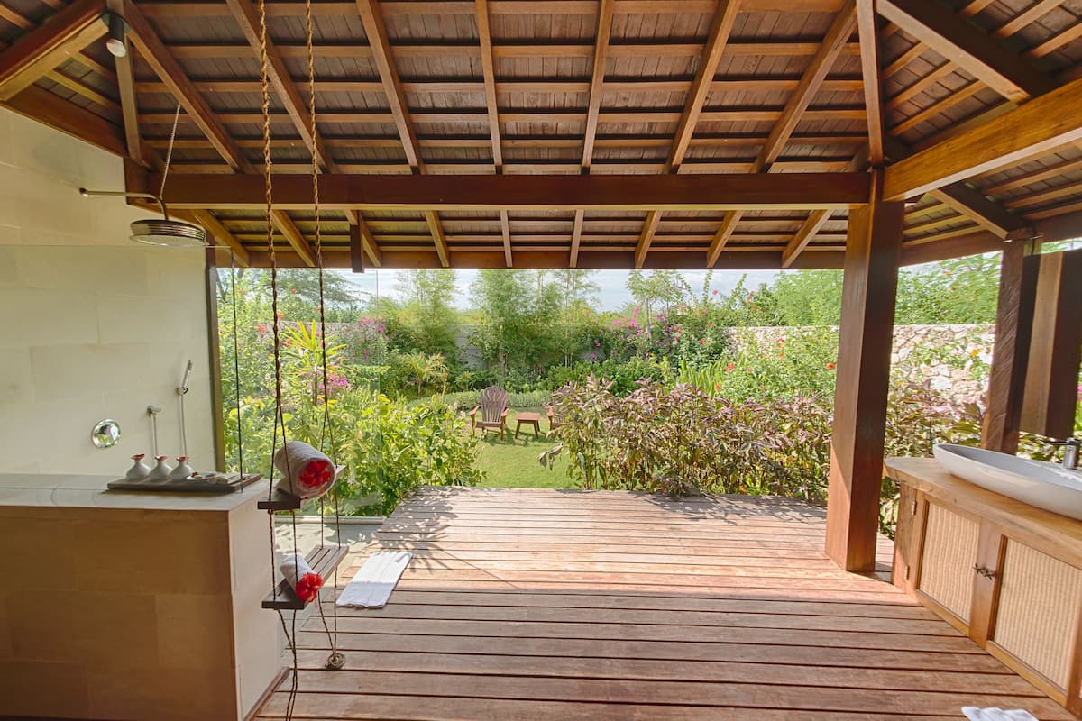 Una terraza de madera con una pérgola, un espacio de descanso y vistas a un jardín.