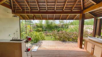A wooden deck with a pergola, a small seating area, and a view of a garden.