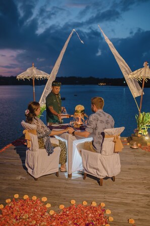 Un espacio de comedor con mesa y sillas en una terraza de madera junto al agua.