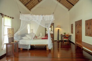 Una habitación con una cama bajo un dosel, un banco de madera, un escritorio con lámpara y puertas de madera.