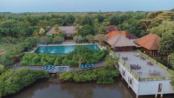 An aerial view of a resort with a swimming pool, lounge chairs, and a thatched-roof building.