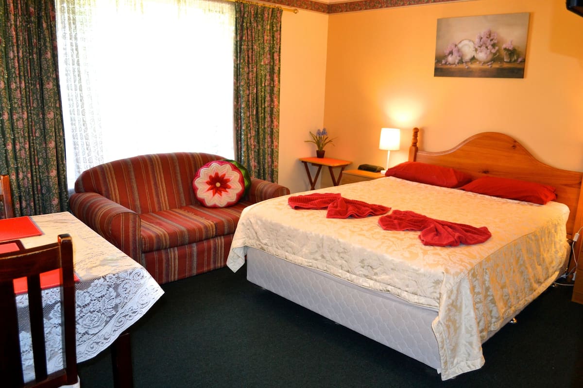 A hotel room with a bed, a chair, a table, a lamp, and a painting on the wall.