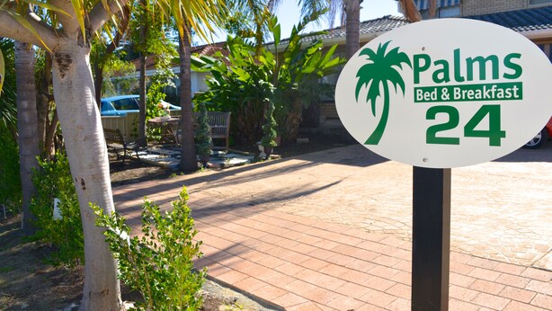 A sign for "Palms Bed & Breakfast 24" with a palm tree logo. - Palms Bed & Breakfast (Warwick)