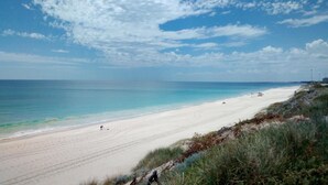 A wide sandy beach with gentle waves, a clear sky, and sparse vegetation along the shore. - Palms Bed & Breakfast (Warwick)