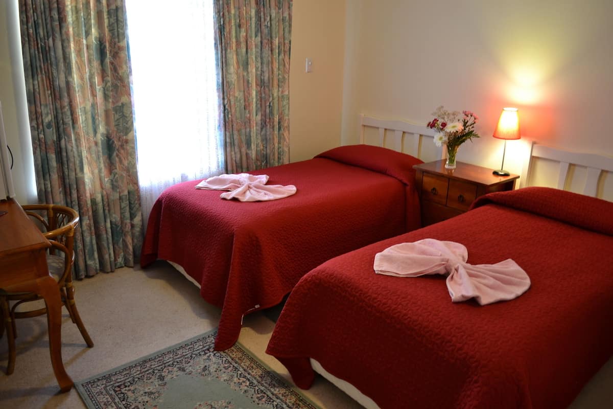 A hotel room with two beds, a wooden chair, a nightstand with a lamp, and a floral vase.