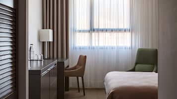 Une chambre d’hôtel avec un lit, un bureau avec une chaise, une lampe et une fenêtre avec des rideaux.