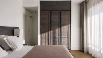 Quarto moderno com cama grande, mesa de cabeceira com luminária e guarda-roupa com acabamento escuro.