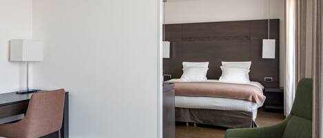 Habitación de hotel con cama, escritorio, silla y mesita de noche.