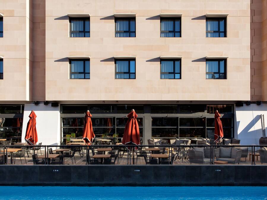 A hotel exterior with a poolside area featuring outdoor seating and umbrellas.