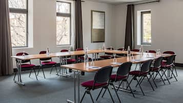 A conference room with long tables and red chairs, large windows with curtains, and a whiteboard on the wall.