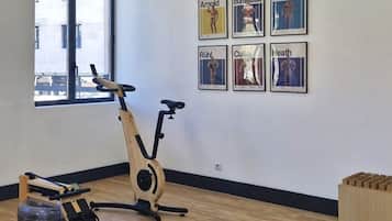 A room with a rowing machine, a standing bike, and a wall with framed pictures.