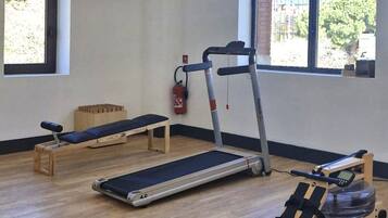 Ett gym med löpband, en roddmaskin och en träningsbänk.