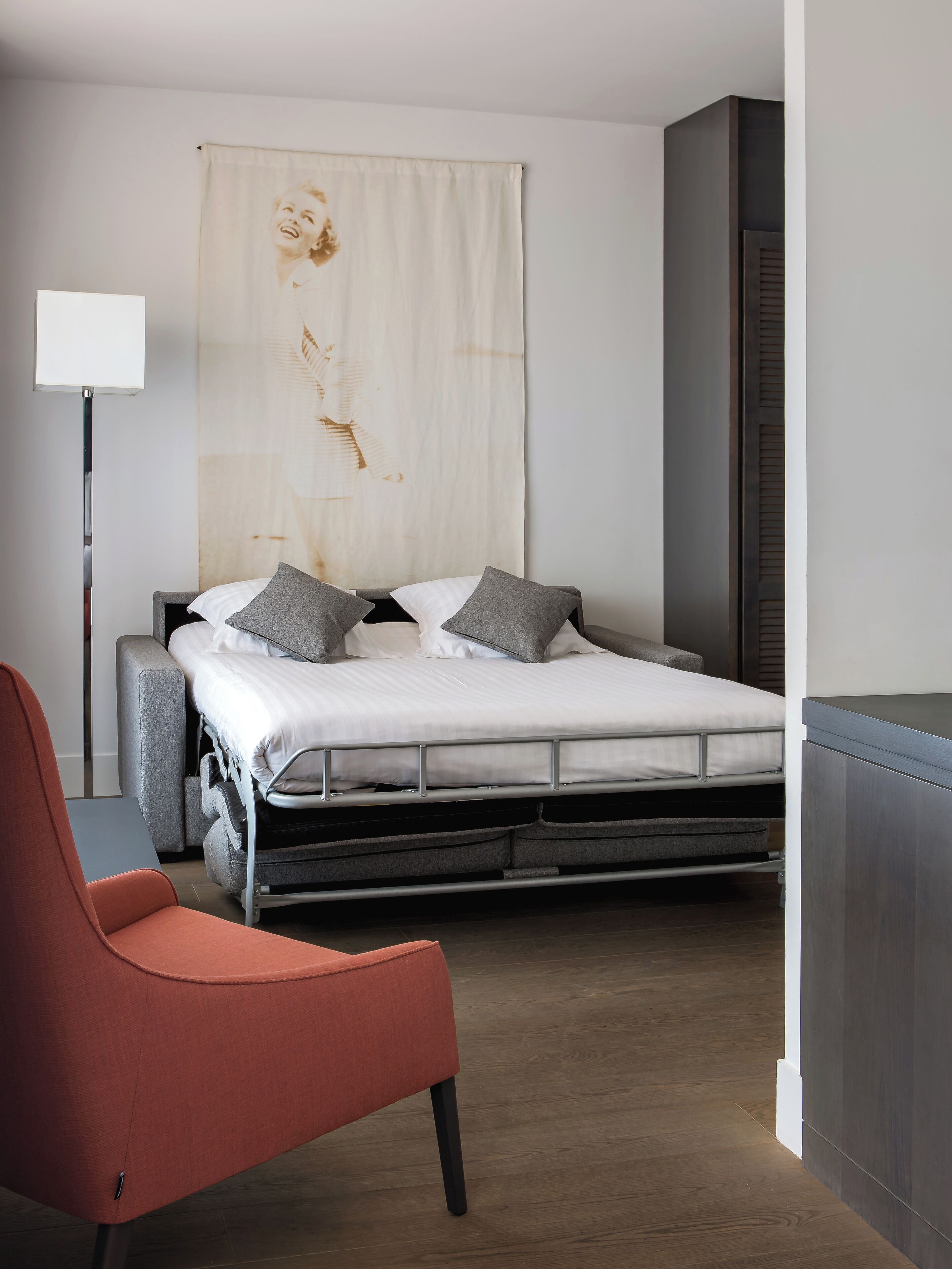 A modern bedroom with a bed, a red chair, and a large artwork on the wall.