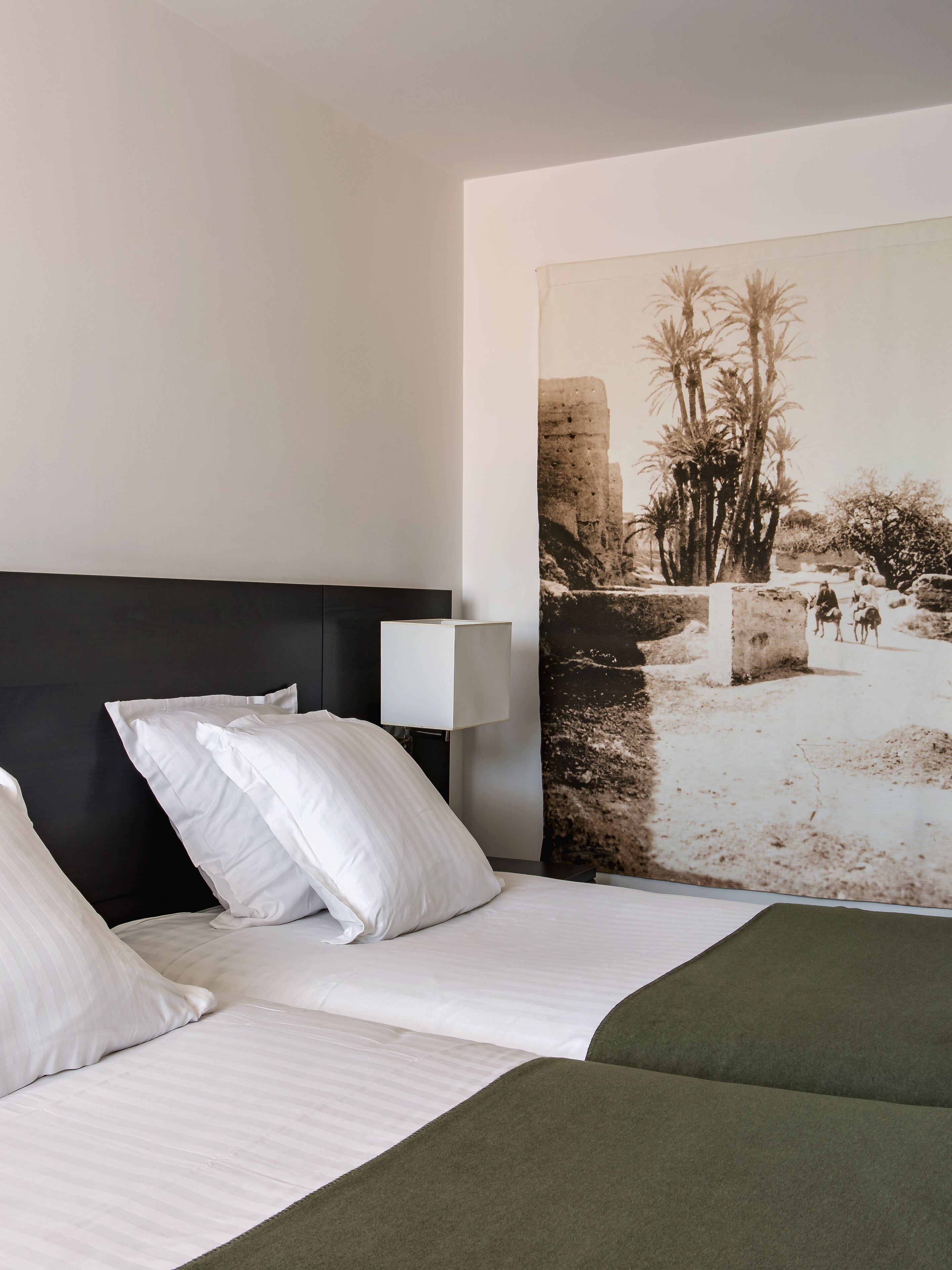 Ein Hotelzimmer mit Bett, Kissen, Nachttisch, Lampe und einer großen Wandmalerei.