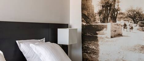 A hotel room with a bed, pillows, a nightstand, a lamp, and a large wall mural.