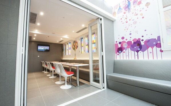 A modern conference room with a glass partition, white chairs, a table, and a colorful abstract wall art. - Inn Hotel Macau (Taipa)