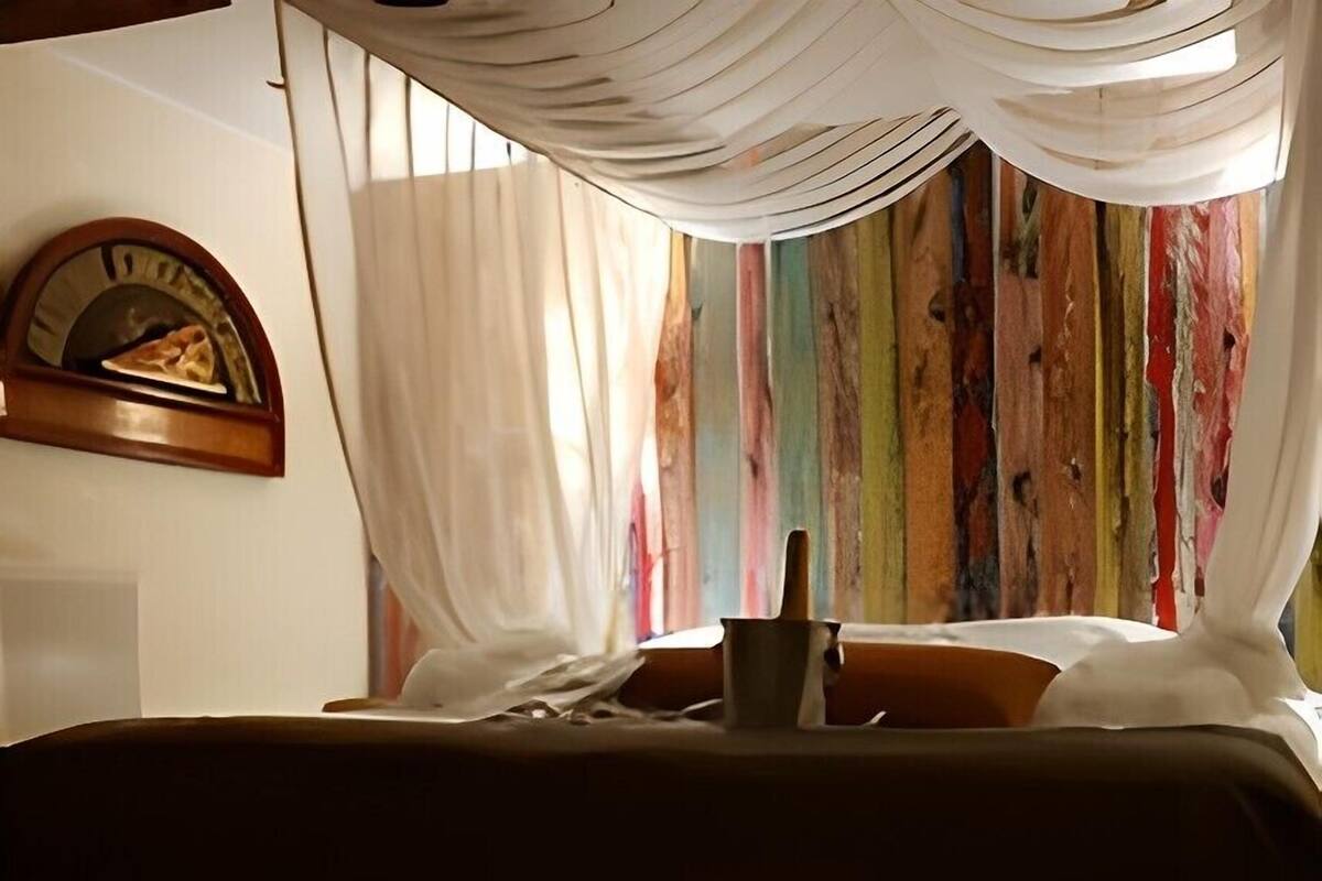 A bed with a white canopy, a wooden headboard, and a colorful striped wall behind it.