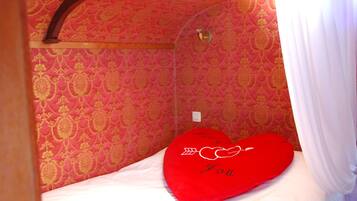 Een kamer met een bed, een rood hartvormig kussen met de tekst 'I love you' en behang met een patroon.