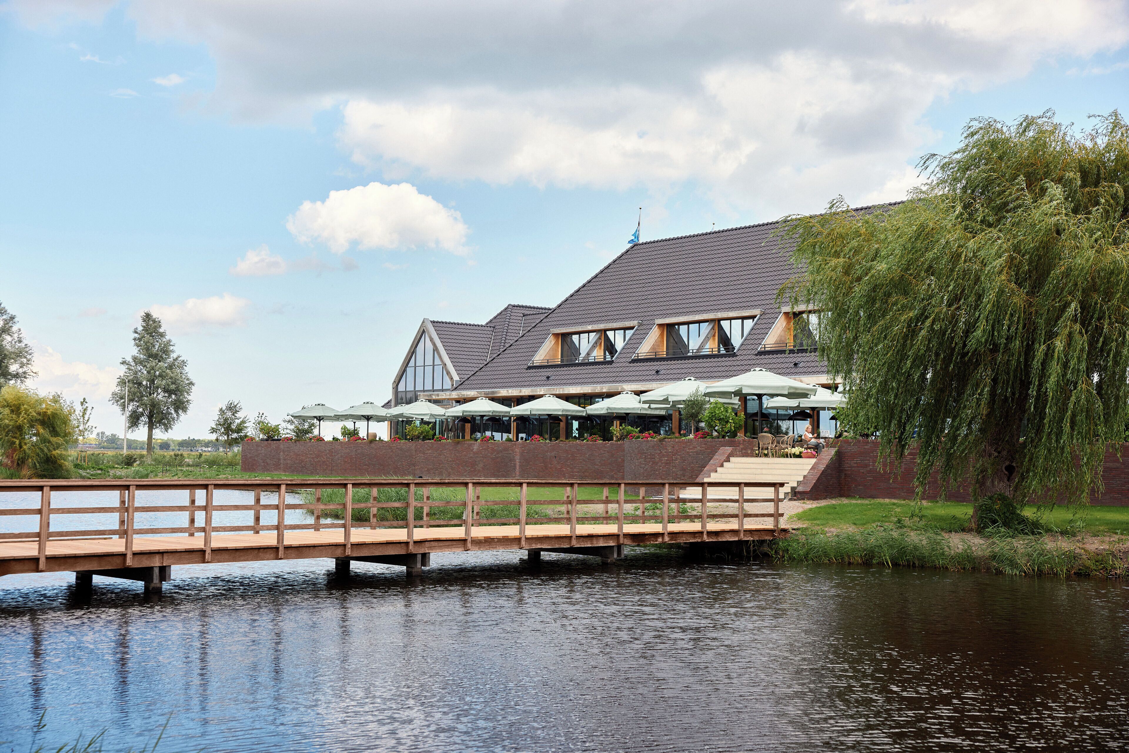 A riverside restaurant with outdoor seating and a wooden bridge.