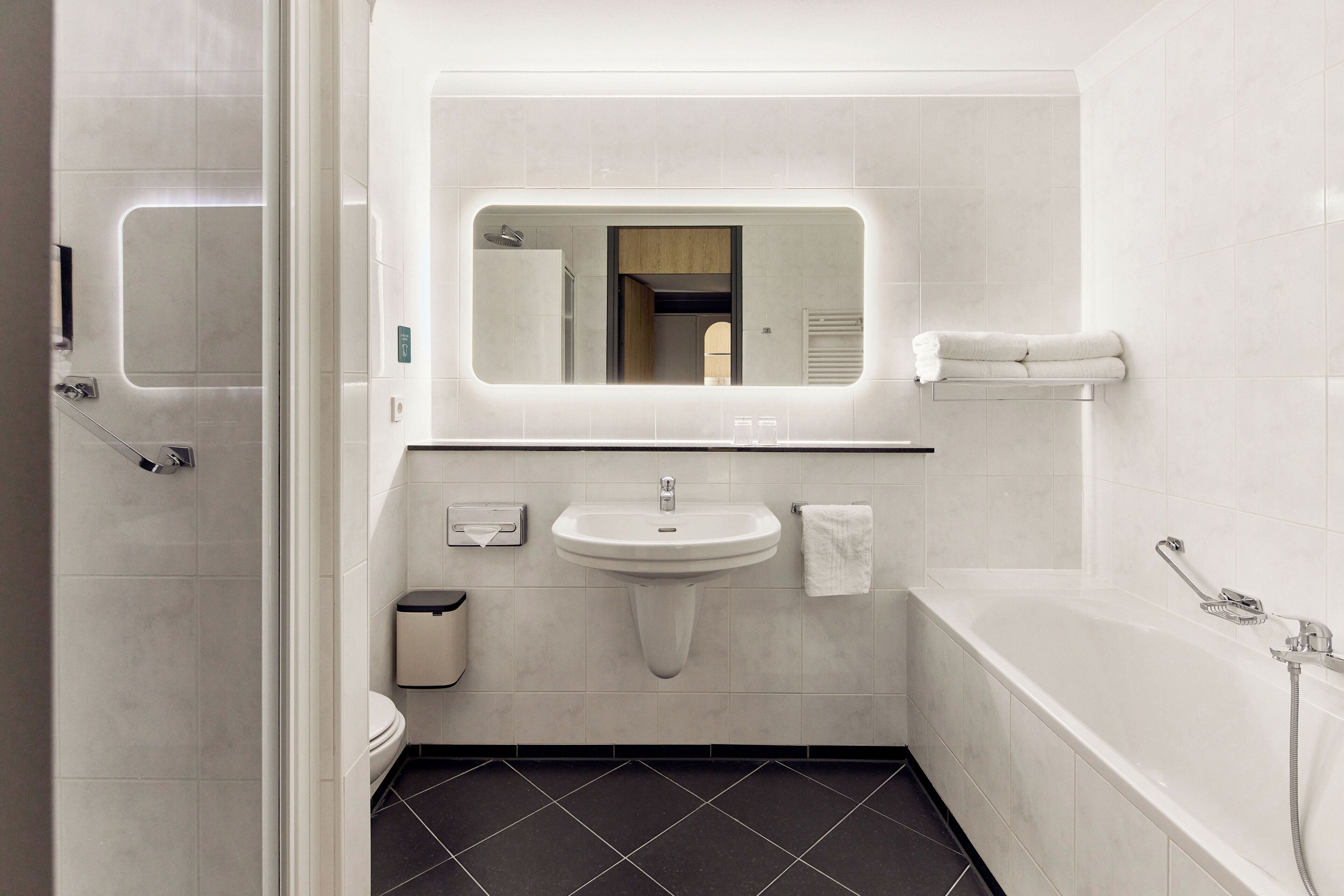 A modern bathroom with a sink, mirror, toilet, and bathtub.