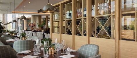 Un restaurant avec des tables rondes dressées pour le dîner, des étagères à vin en bois en arrière-plan et un éclairage moderne suspendu au plafond.