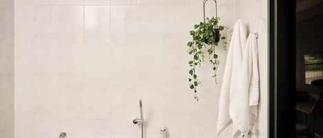 A bathroom with a bathtub, a shower, and a hanging plant.