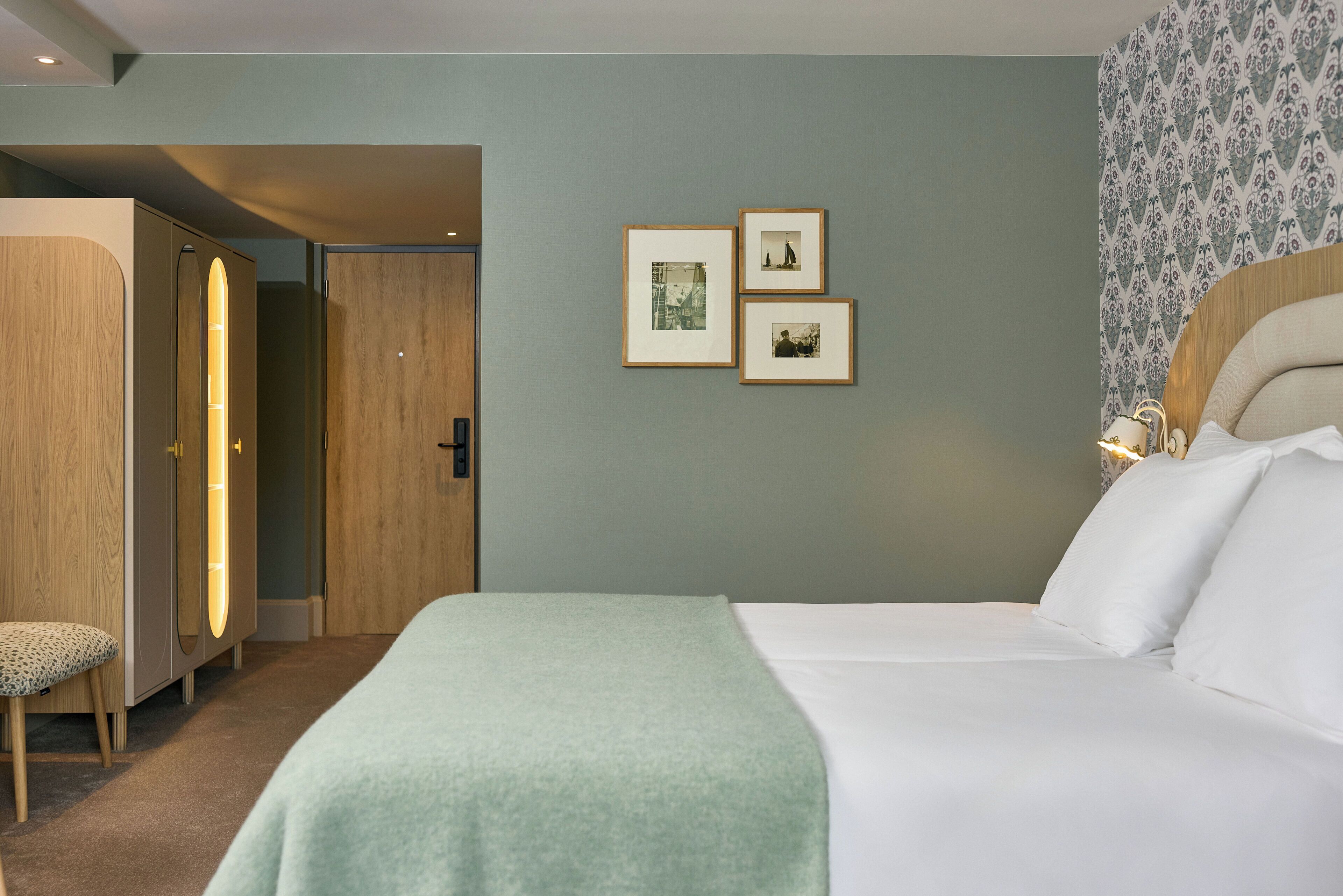 Une chambre d’hôtel avec un lit, une armoire en bois, un banc et des tableaux encadrés accrochés au mur.