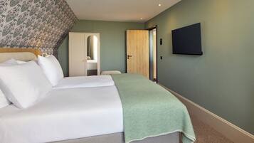 A bedroom with a bed, a green blanket, a wooden door, and a wall-mounted TV.