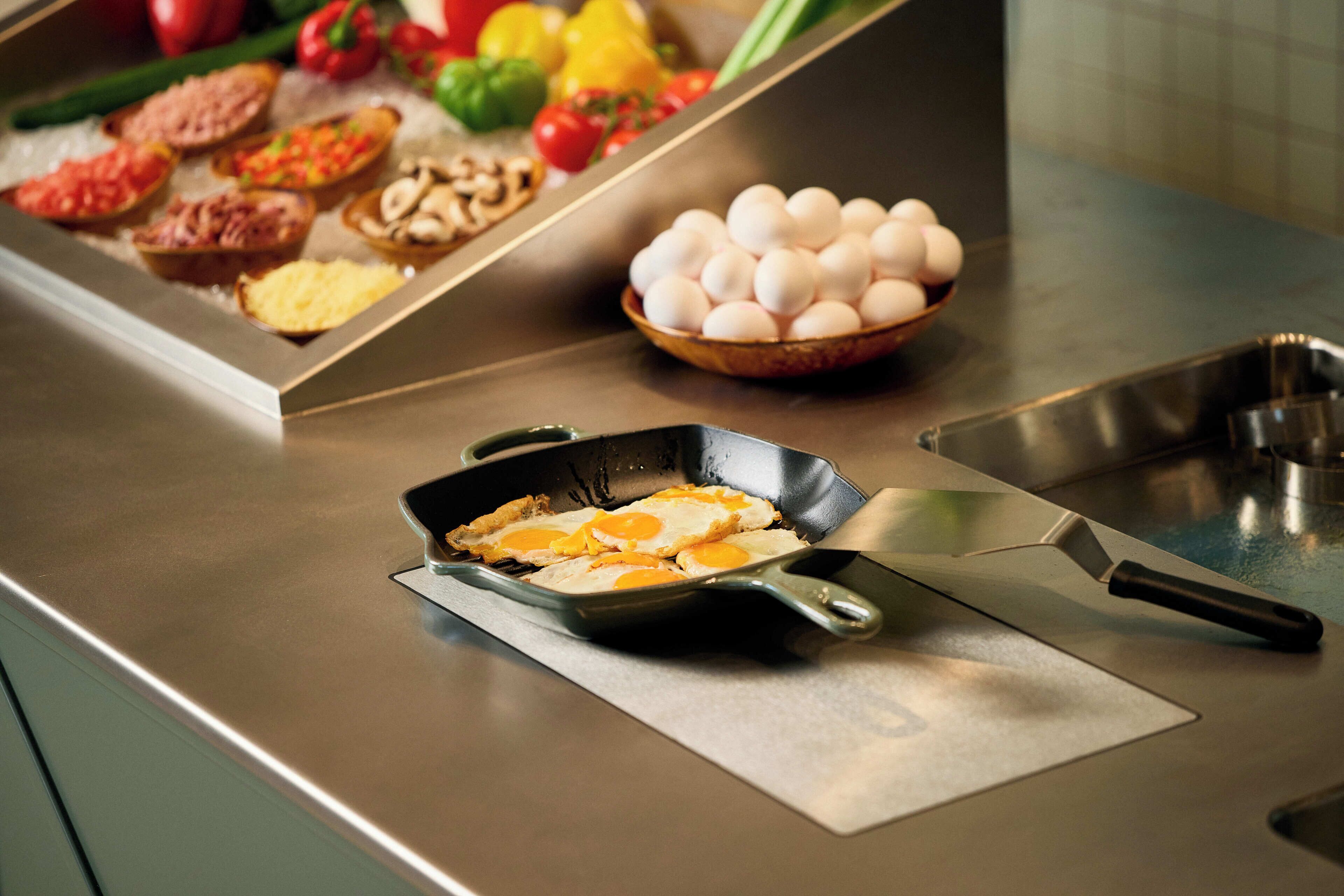A kitchen counter with a frying pan containing eggs, a bowl of eggs, and various food items.