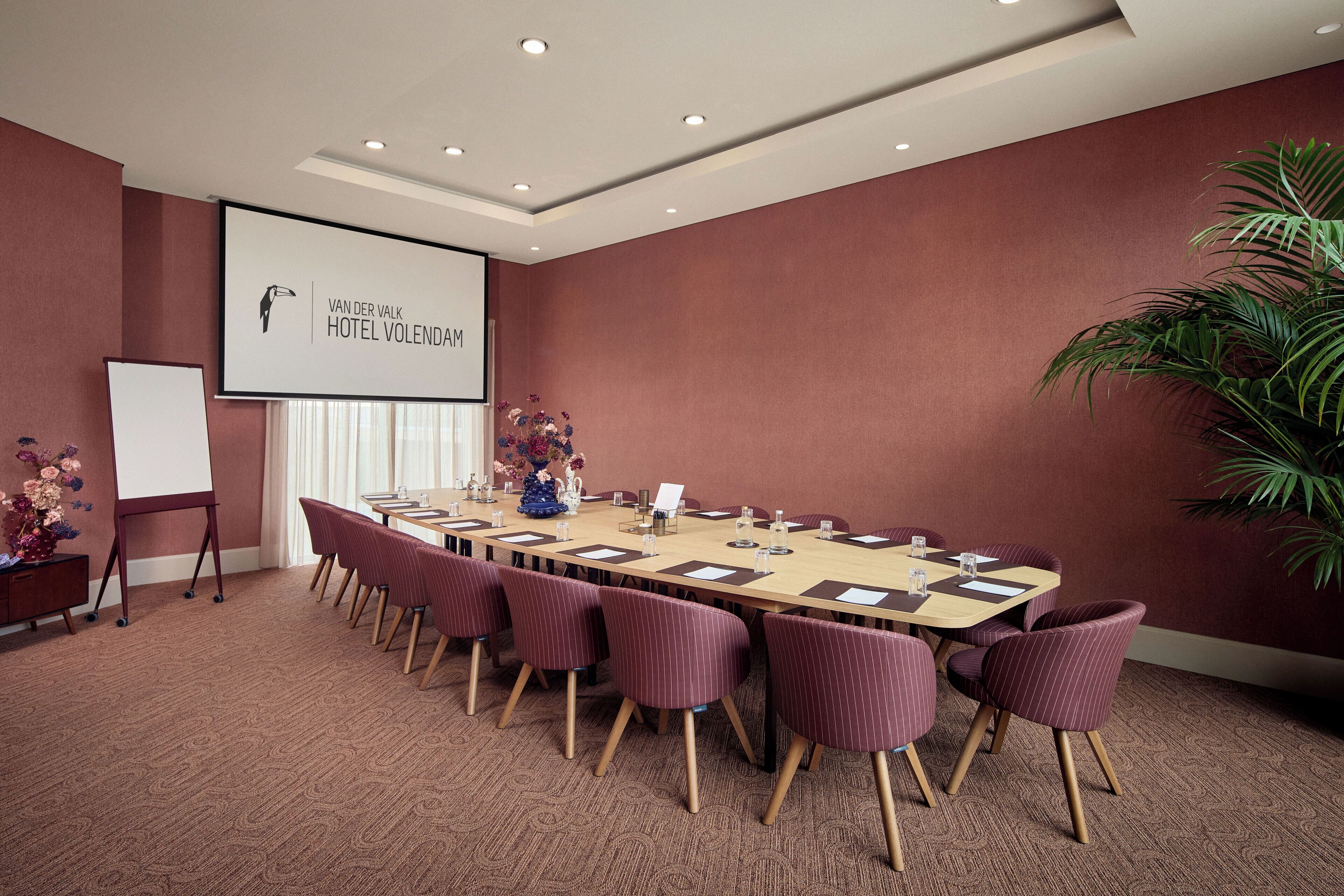 Un salón de conferencias con una larga mesa, sillas, una pantalla de proyector y una pizarra.