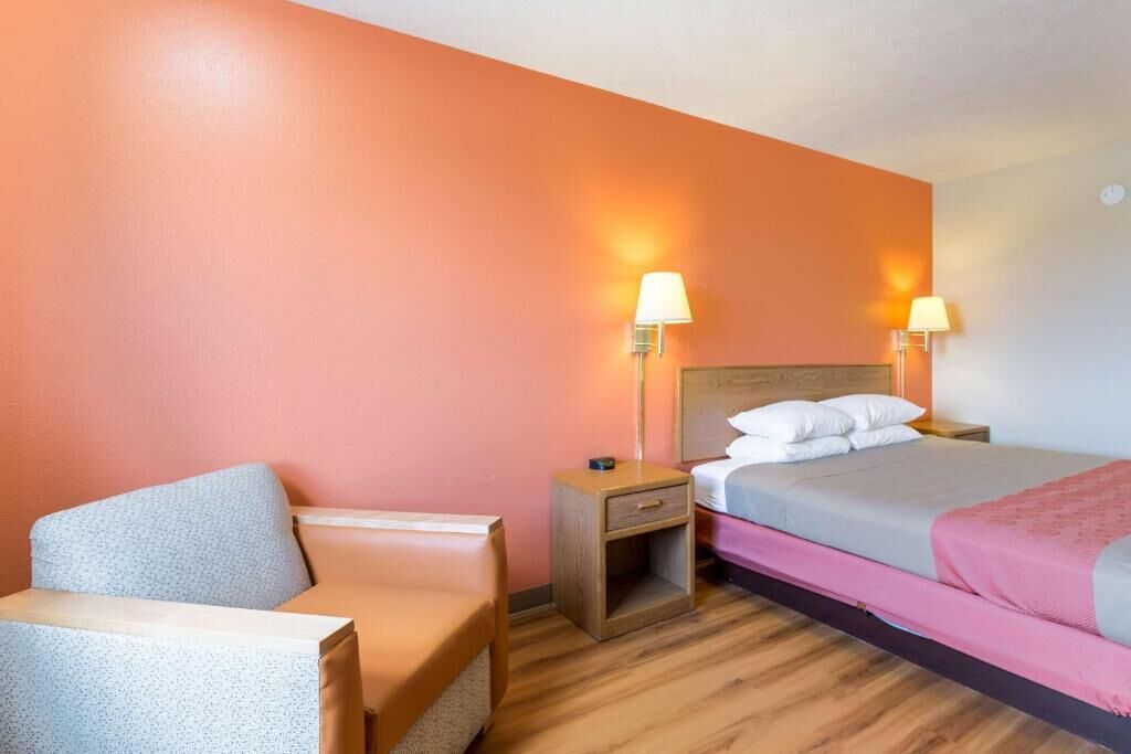 A hotel room with a bed, bedside tables, a chair, and a lamp.