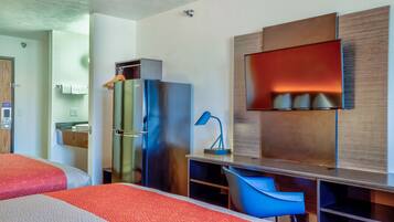 A modern hotel room with two beds, a refrigerator, a desk with a chair, a TV, and a bathroom visible in the background.