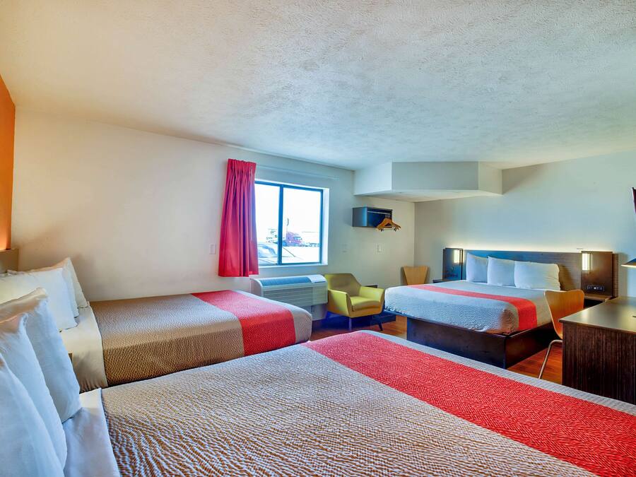 A hotel room with two beds, a window with curtains, a desk, and a chair.