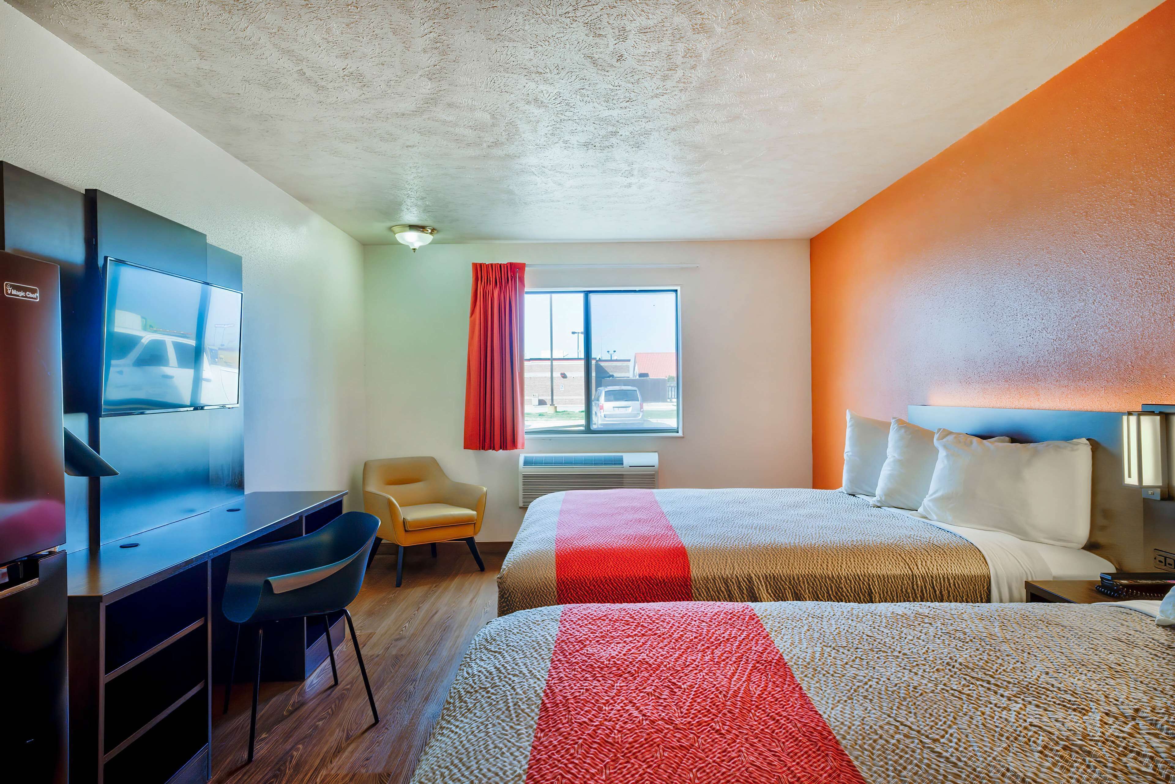 Ein Hotelzimmer mit Bett, Schreibtisch mit Stuhl, Fernseher und einem Fenster mit Vorhängen.