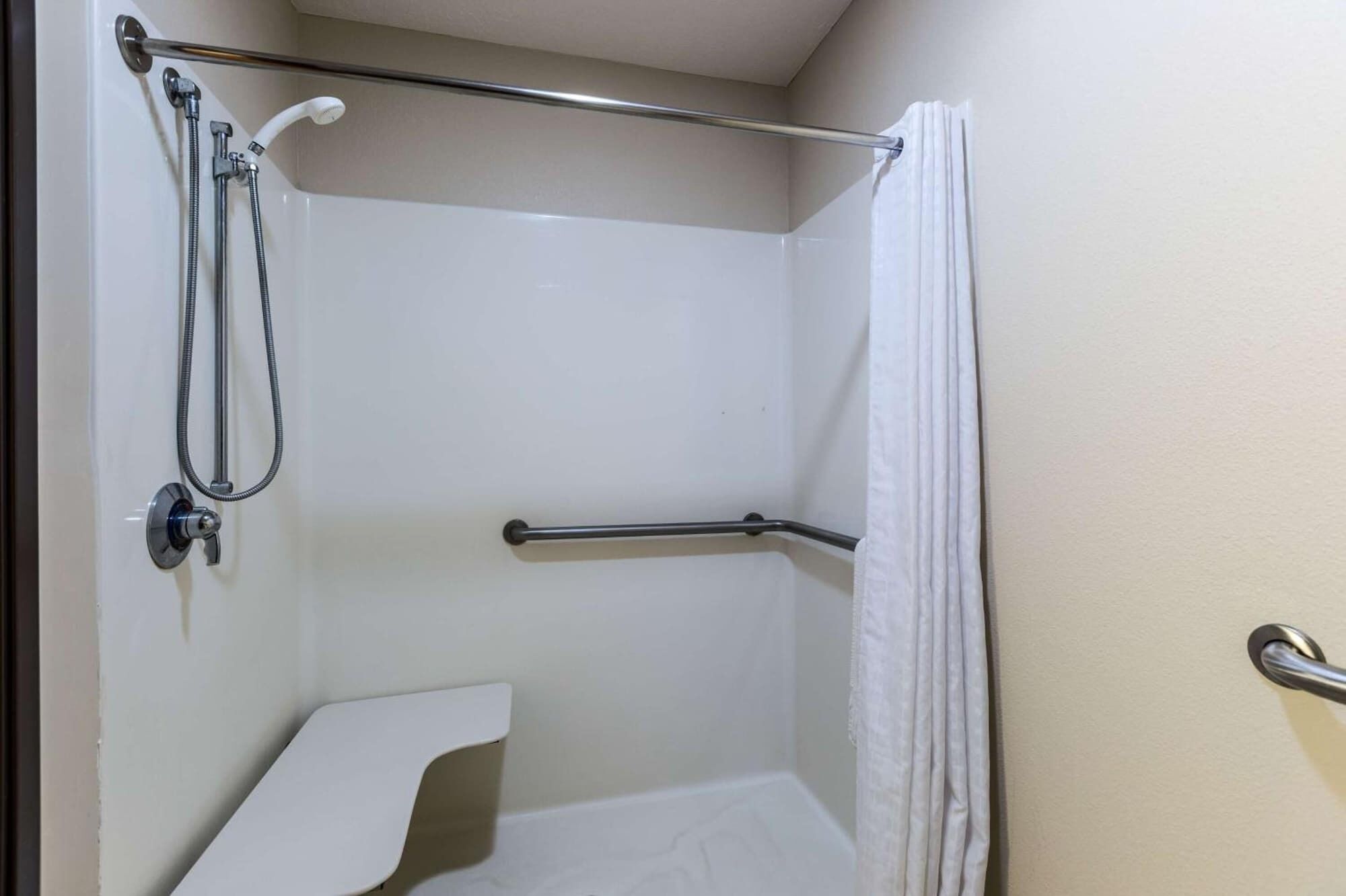 A small, enclosed shower area with a grab bar, a toilet, and a showerhead.