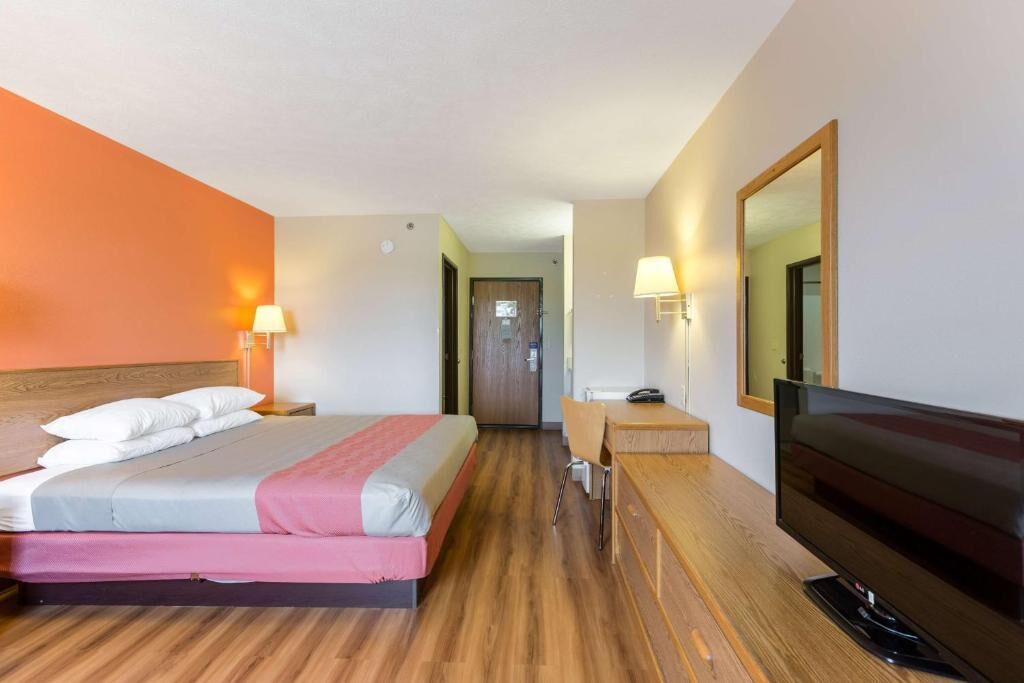 A hotel room with a bed, bedside lamps, a desk with a chair, a TV, and a mirror.